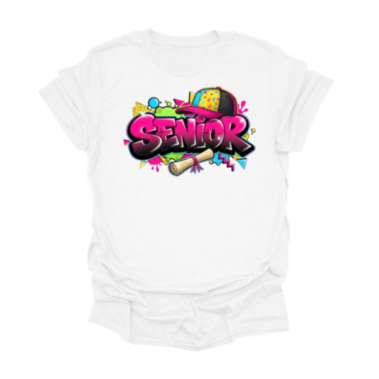 White senior graphic t-shirt featuring bold colorful Senior text with graduation themed design including diploma illustration and vibrant decorative elements.